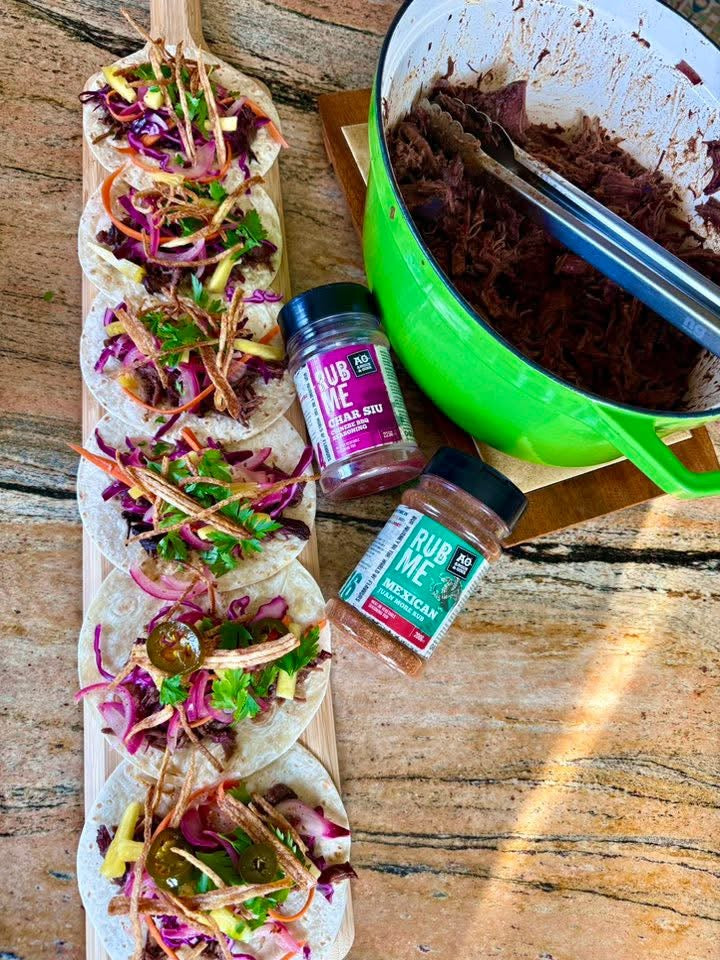 Tacos with colorful toppings on a wooden surface, accompanied by two seasonings subs from angus & oink