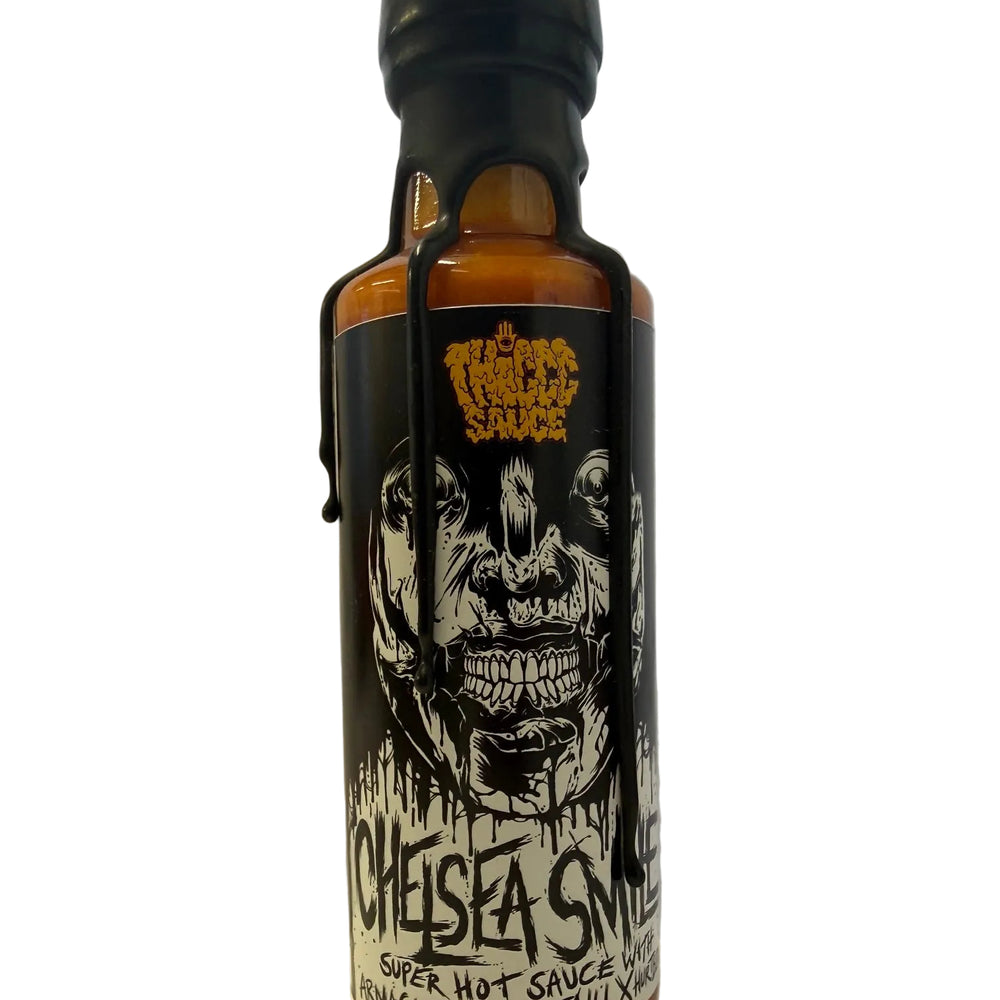 A bottle of Anaheddon x Fatih X Chelsea's Super Hot Sauce, featuring a black label with a white skull graphic and dripping design, topped with a black cap and black wax dripping down the sides, set against a plain light background.