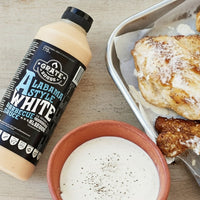Baked chicken wings with a bottle of Grate Goods Alabama White barbecue sauce on a wooden surface.