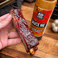 Sliced meat with a bottle of sauce on a wooden cutting board