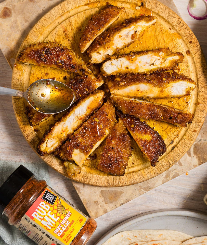 Fried chicken pieces on a wooden board with tortillas, salad, and condiments on a table.
